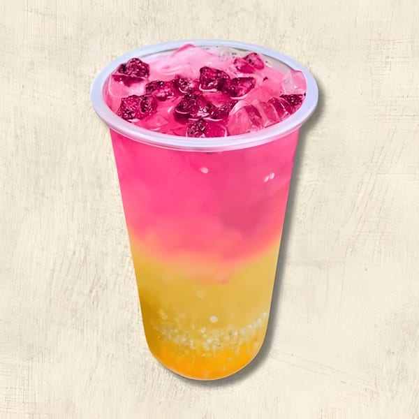 A vibrant pink and yellow layered drink with ice and dark red fruit pieces in a clear plastic cup.